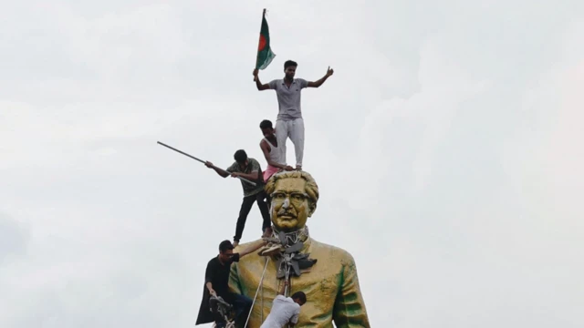 प्रधानमंत्री आवास में लगी बांग्लादेश के संस्थापक और शेख़ हसीना के पिता शेख़ मुजीबुर्रहमान की विशाल मूर्ति पर प्रदर्शनकारी चढ़ गए. हथौड़े से इस मूर्ति को तोड़ने की कोशिश की गई.