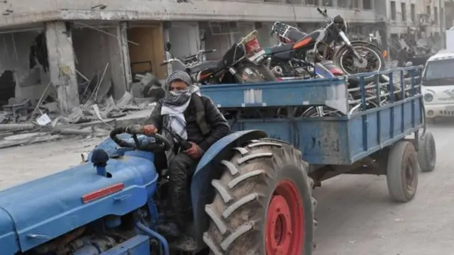 رجل يقود جرارا زراعيا وعربة مليئة بالمنهوبات