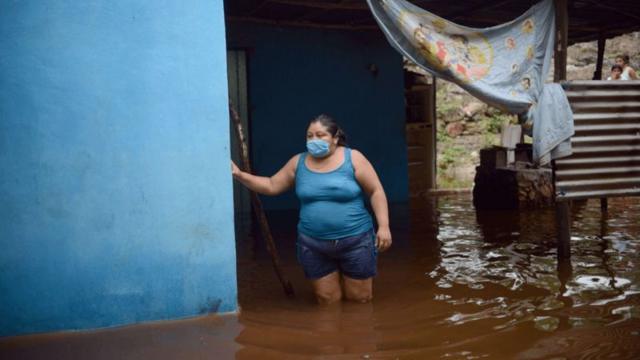 Mujer caminando en una calle inundada con al agua a la altura de las rodillas