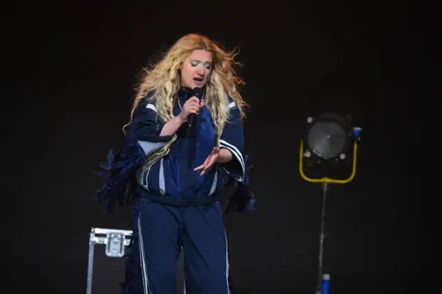 певачица у тегет спортском комплету, плаве косе, затворених очију пева