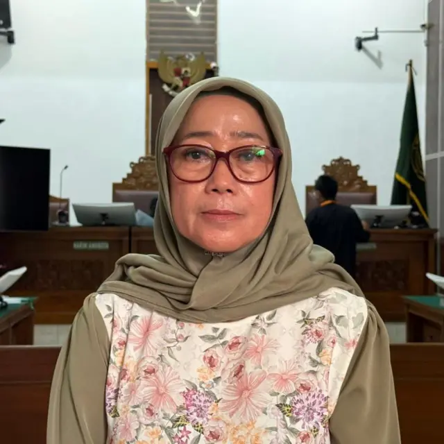 Seorang perempuan berhijab berdiri di depan pintu sebuah pengadilan.