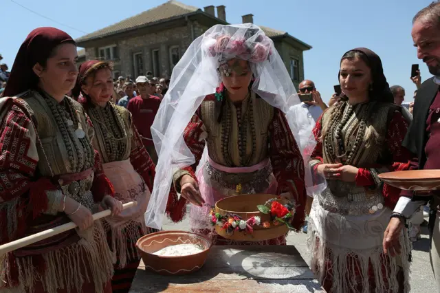 Mladu dočekuje svekrva sa pogačom, bokalom vina i sitom. Nakon što je skinula veo, ona prosejava brašno.