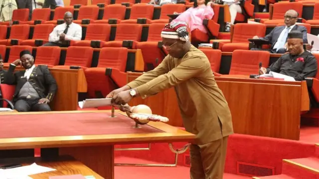 sẹnetọ kan n fi iwe abadofin lelẹ niwaju ọpa aṣẹ̀ ile naa