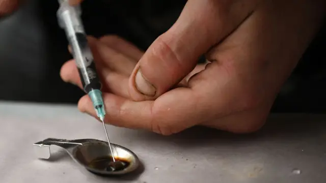 Unas manos con una aguja hipodérmica y una cuchara con una dosis de heroína