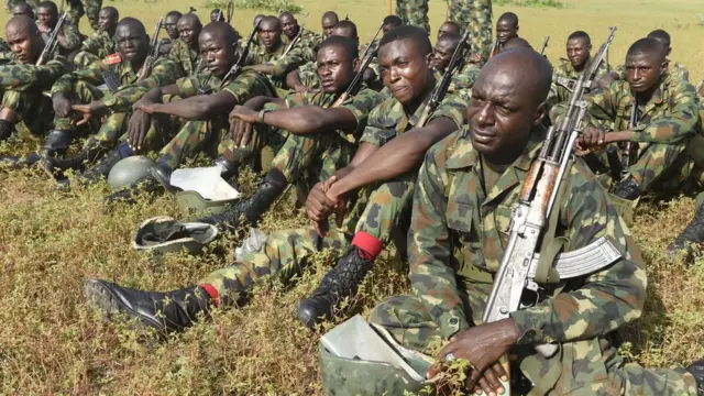 Awọn ologun joko lori papa pẹlu ibọn wọn lọwọ