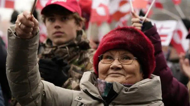 عدد من المتظاهرين وتظهر إحدى المتظاهرات مرتدية معطفاً وقبعة حمراء اللون.