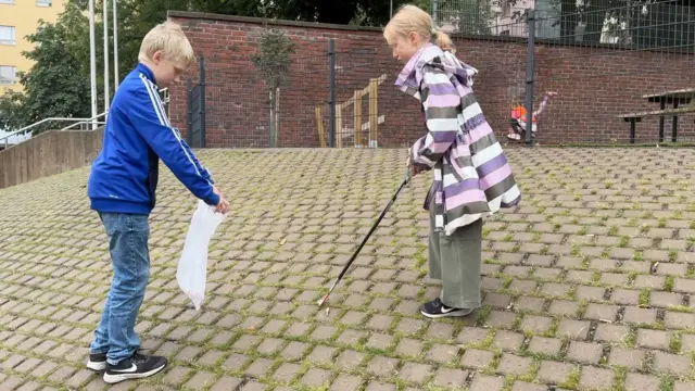 یک پسر و یک دختر با هم در زمین بازی مکتب آشغالها را جمع می کنند. پسر کیسه‌ای را باز نگه داشته است و دختر از زباله جمع کن استفاده می‌کند