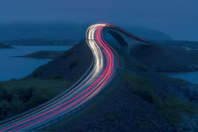 Luces de los autos transitando una carretera que se alza y sobre el agua