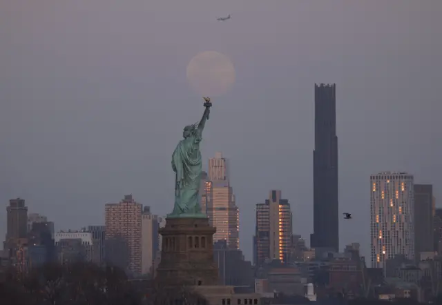Di moon dey behind di Statue of Liberty and di Brooklyn Tower for New York City