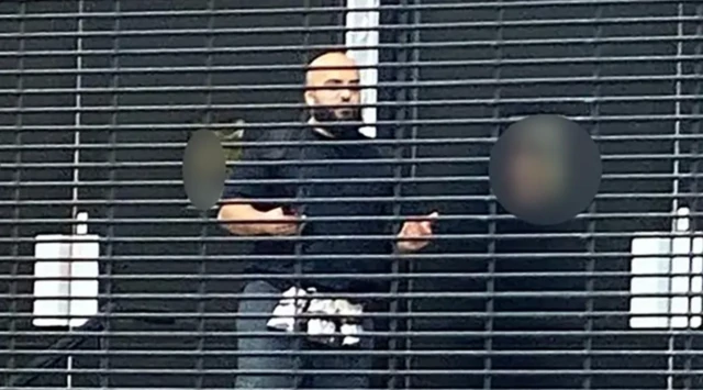 Kel ve sakallı bir adam elleri açık şekilde uzaktan görünüyor