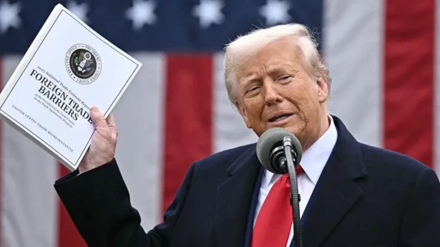 دونالد ترامپ کتابچه موانع تجارت جهانی را در دست گرفته جلوی دوربین نشان می‌دهد