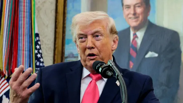 マイクの前で話すスーツ姿のトランプ氏。背後にはレーガン大統領の肖像画が飾られている