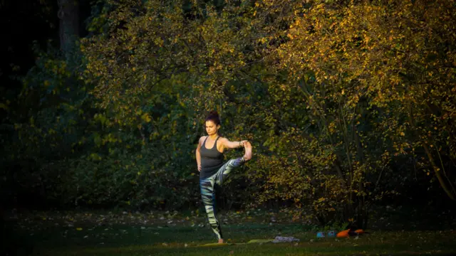 Kobieta ćwiczy jogę, za nią znajdują się drzewa