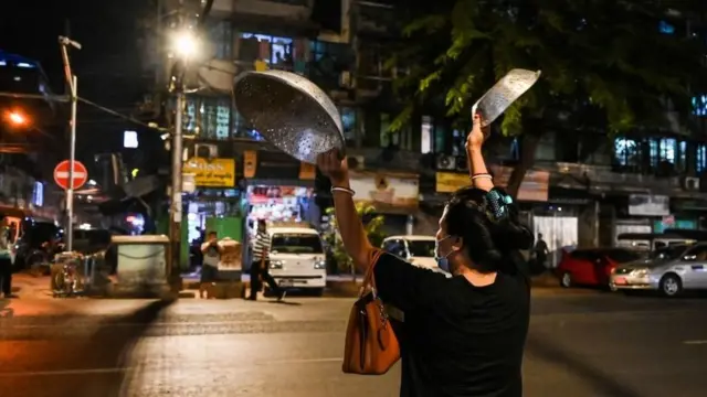A woman clatters pans to make noise after calls for protest went out on social media in Yangon