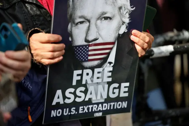 Pessoa segura cartaz com fotoblaze jogo do blazeAssange, pedindo que ele não seja extraditado para os EUA 