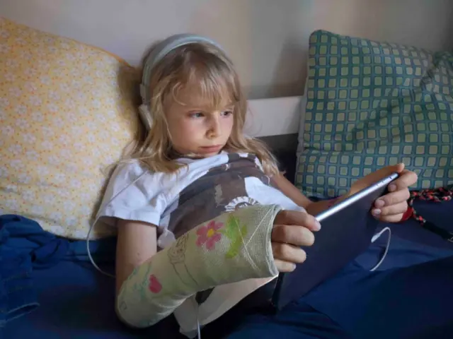 Uma criança sentada na cama com fones de ouvido e um iPad na mão
