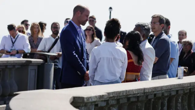 William conversando com um grupo de pessoas. Ao fundo, várias pessoas olhando