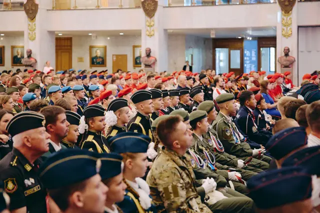Діти у військовій формі сидять у концертному залі.