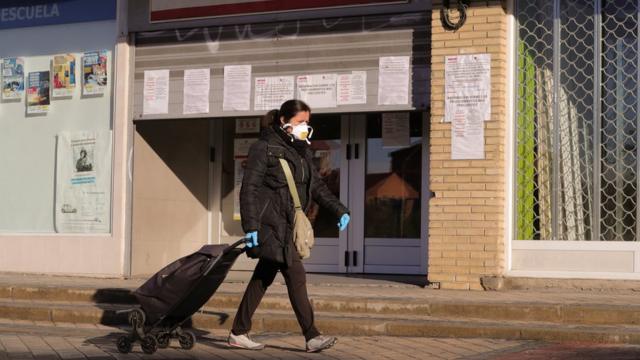 A woman protected with a mask and gloves walks past a public employment office