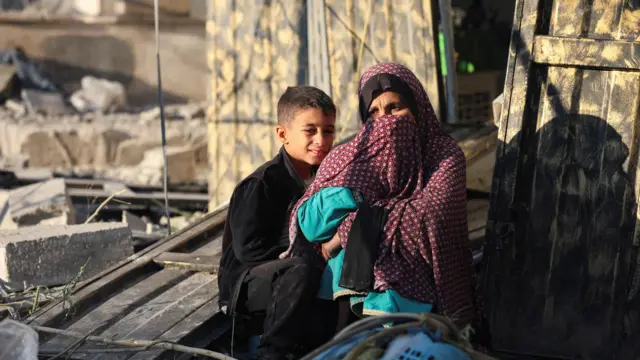 إمرأة غزية مع طفلها أمام بيتهما المهدود في مخيم النصيرات