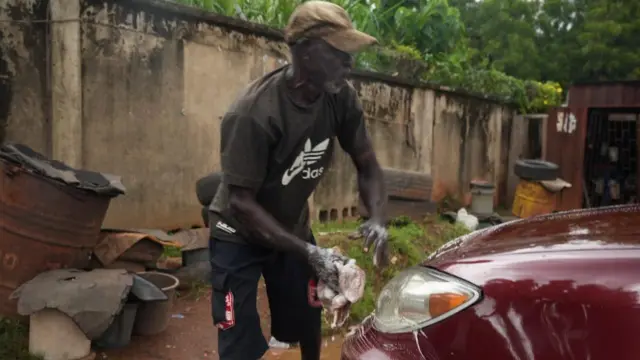 Emeka Ede, 70, washing a red-colour car at Ochomma car wash, Enugu Nigeria 
