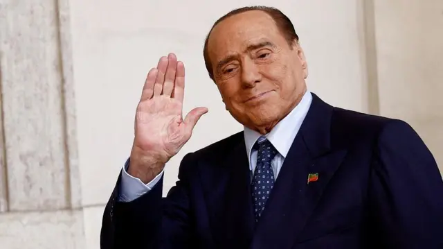 Berlusconi acenando e sorrindo contidamente