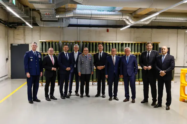 На открытии нового завода Rheinmetall по производству артиллерийских боеприпасов в Унтерлюсе, Германия, для совместной фотографии позируют генсек НАТО Марк Рютте, министр обороны Германии Борис Писториус, президент Болгарии Румен Радев, глава Rheinmetall Армин Паппергер и другие официальные лица. Снимок сделан внутри предприятия на фоне артиллерийских снарядов 27 августа 2025 года.