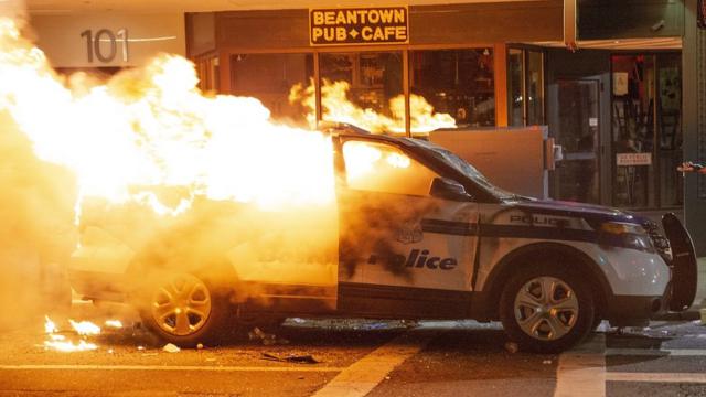 抗议者据报不断向波士顿的防暴警察投掷瓶子，然后将一辆警车付之一炬。