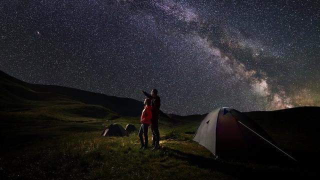 A father and a child, camping, admiring the starry night sky