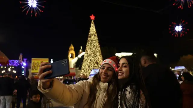 Two women take foto for front of di Christmas tree for Nativity Square for Bethlehem, hold to be di birthplace of Jesus Christ, for di occupied West Bank