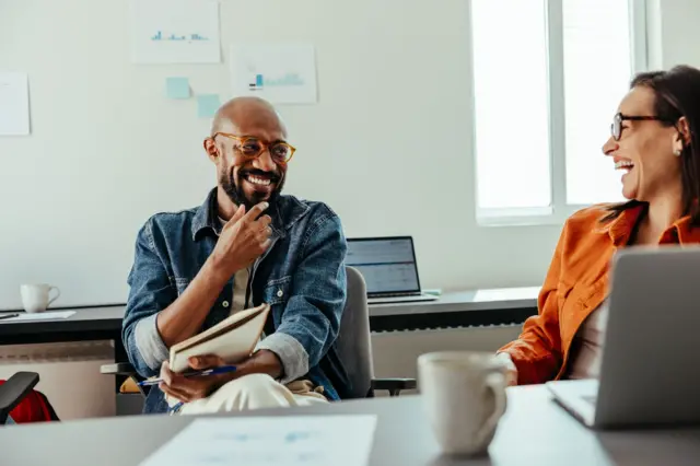 Gözlüklü siyah bir adamlar bir kadın birbirlerine bakarak gülüyorlar.