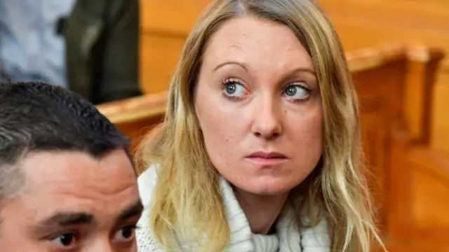 Foto de Laura Temperault, uma mulher de cabelos, olhos e pele clara, em um tribunal. 
