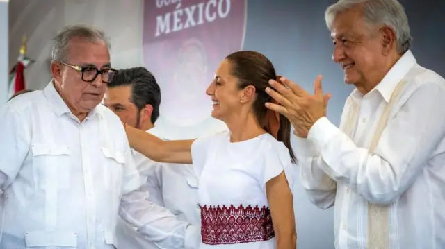 La presidenta de México coloca su brazo sobre el gobernador Rocha Moya, mientras que AMLO aplaude.