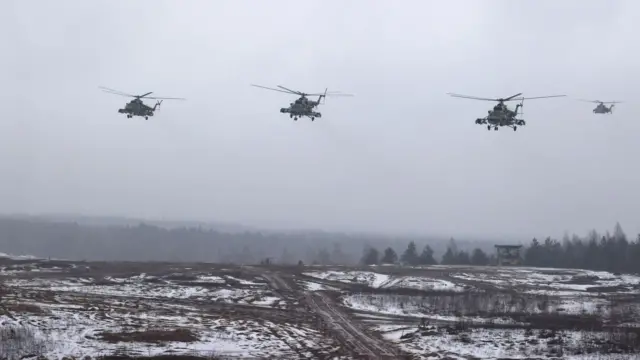 Cztery białoruskie śmigłowce szturmowe przelatują nad pokrytym śniegiem krajobrazem, w tle widać spowity mgłą las.