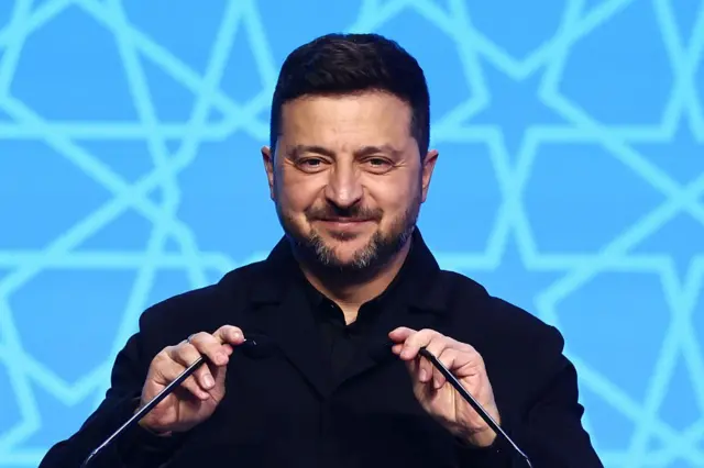 Зеленський тримає руками два мікрофони перед собою і посміхається