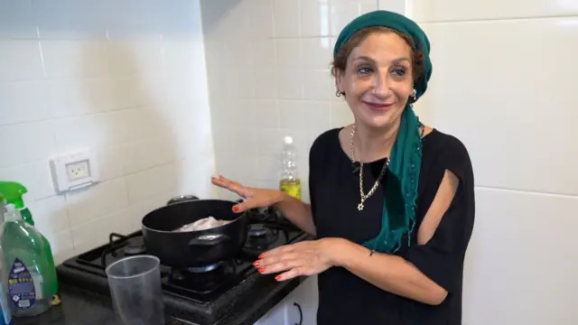 Una mujer, vestida de negro, junto a la olla en que cocina la comida para su familia. 
