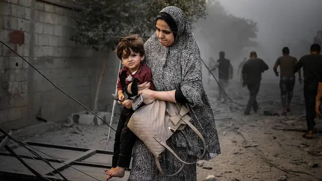 Madre cargando su niño pequeño en una calle con escombros