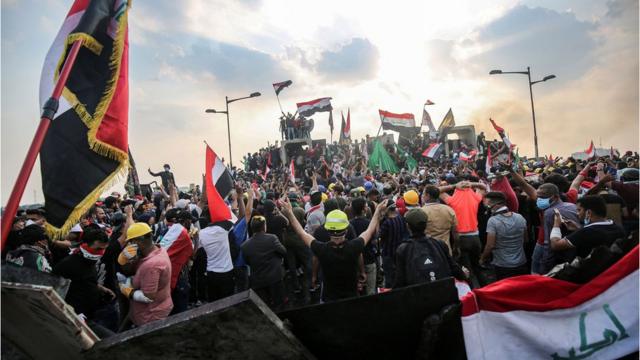 Iraqi protesters wave national flags as they stand atop concrete barriers across the capital Baghdad"s al-Jumhuriya bridge which connects between Tahrir Square and the high-security Green Zone, hosting government offices and foreign embassies, on October 29, 2019 during the ongoing anti-government protests.
