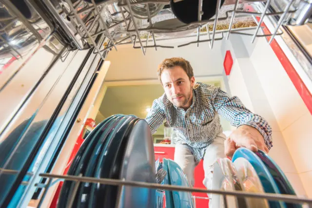 bir erkek eğilmiş halde yıkanmış kaplarla dolu bulaşık makinesine bakıyor