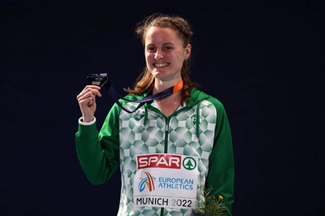 Ciara Mageean sorrindo ao levantar medalha pendurada no pescoço