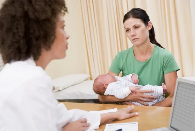 Mujer con bebé en brazos en una consulta médica.