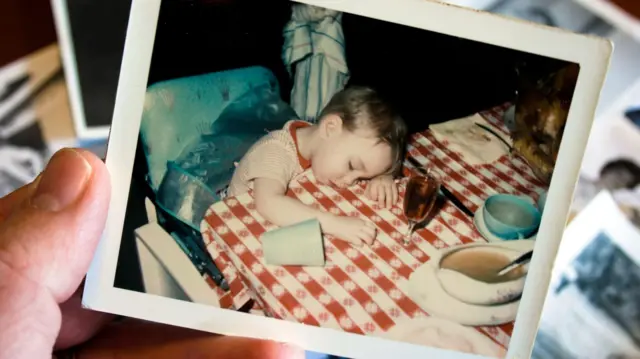 Mão segura foto polaroidibet especializaçãocriança dormindo após refeiçãoibet especializaçãocima da mesa