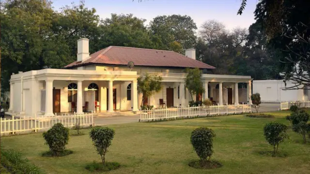 Cottages with cream-coloured walls and verandahs, inside the premises of the Delhi Gymkhana Club, in front of green and wide fenced lawns.