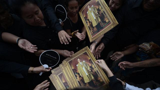 Mourners are handed pictures of the late king