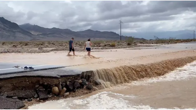 Um homem e uma mulher caminham por uma rua inundada no Vale da Morte.