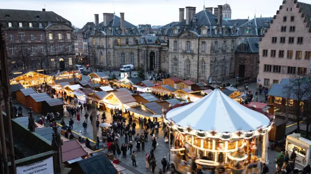 Zwiedzający przechadzają się uliczkami jarmarku bożonarodzeniowego w Strasburgu 
