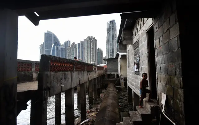 Un niño observa en una casa humilde de Panamá con modernos rascacielos de fondo