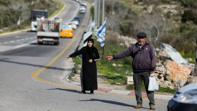 فلسطينيون يشيرون إلى سيارات قرب بوابة إسرائيلية مغلقة في قصرة بالضفة الغربية المحتلة، 5 فبراير/شباط 2026.