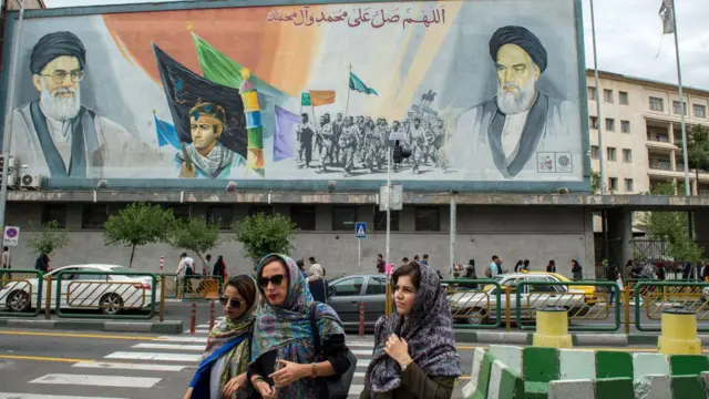 Женщины переходят улицу рядом с гигантским политическим граффити, изображающим аятоллу Хаменеи (слева) и основателя Исламской республики Рухолла Хомейни, в Тегеране