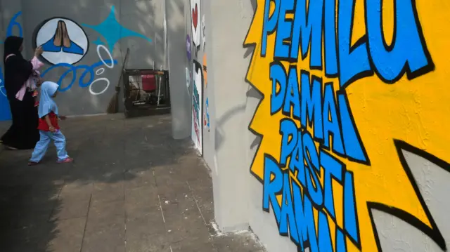 Warga berjalan di depan mural bertema pesan damai untuk Pemilu 2024 di Taman Corat Coret, Kota Bogor, Jawa Barat, Sabtu (22/07).